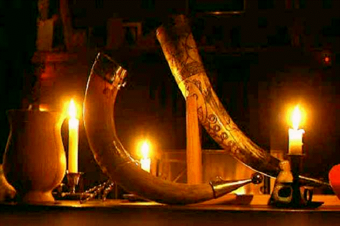 Candles, a jug of mead, and two drinking horns rest on a Yule stalli (altar).